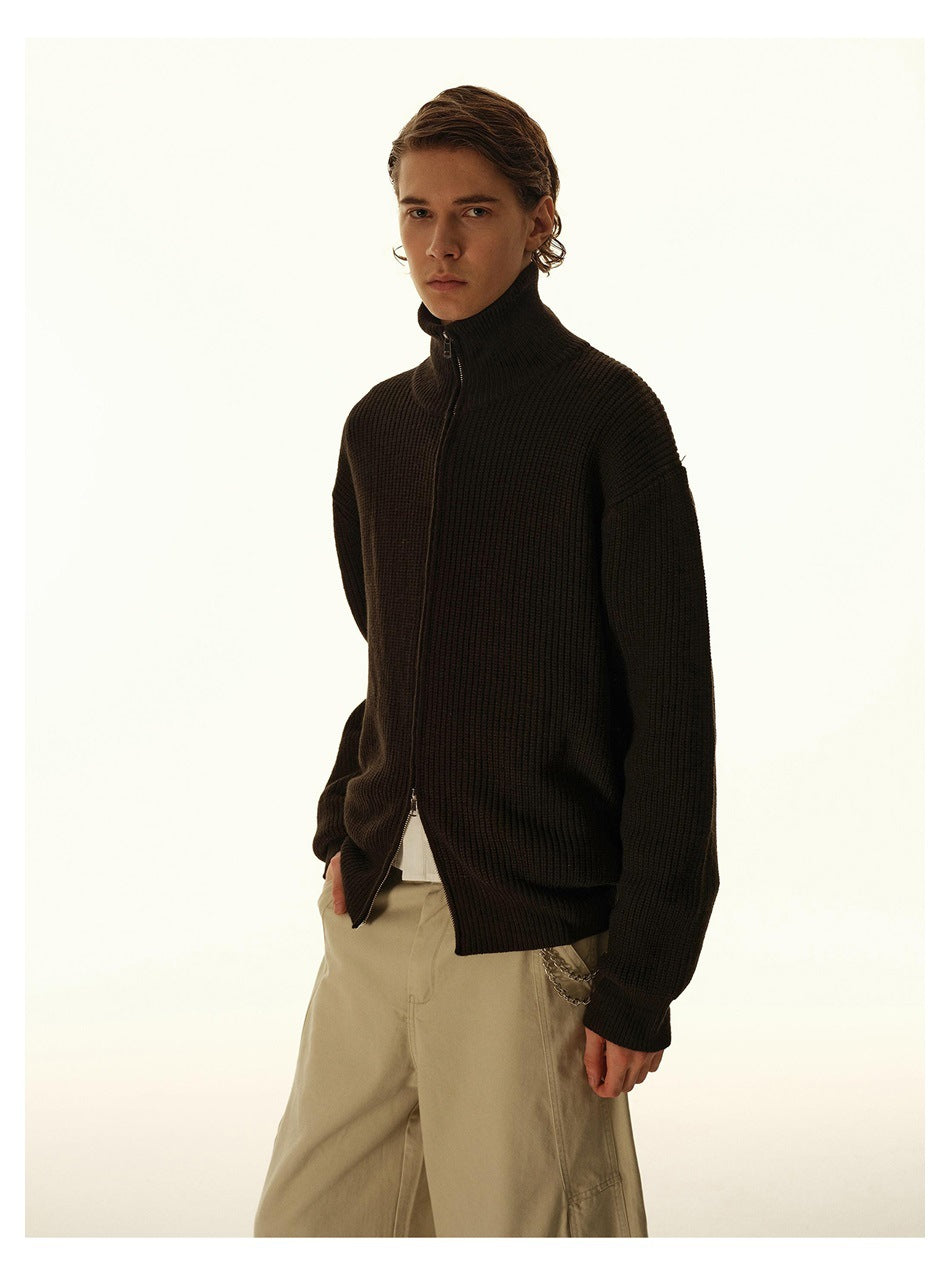 Model wearing a dark brown ribbed zip-up cardigan with a high collar and loose beige trousers.