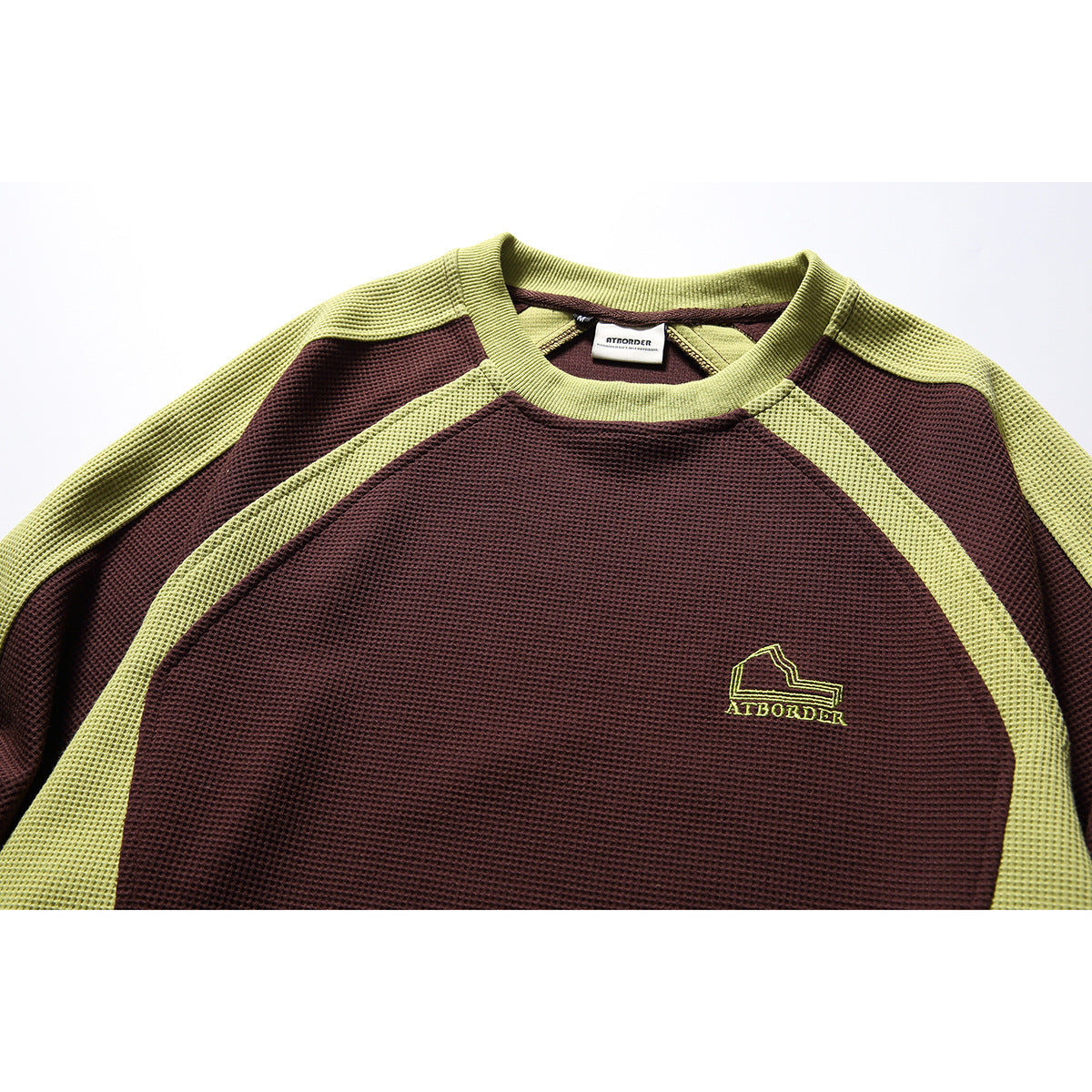 Close-up of a burgundy raglan sweatshirt with lime-green panels, ribbed collar and small chest emblem.