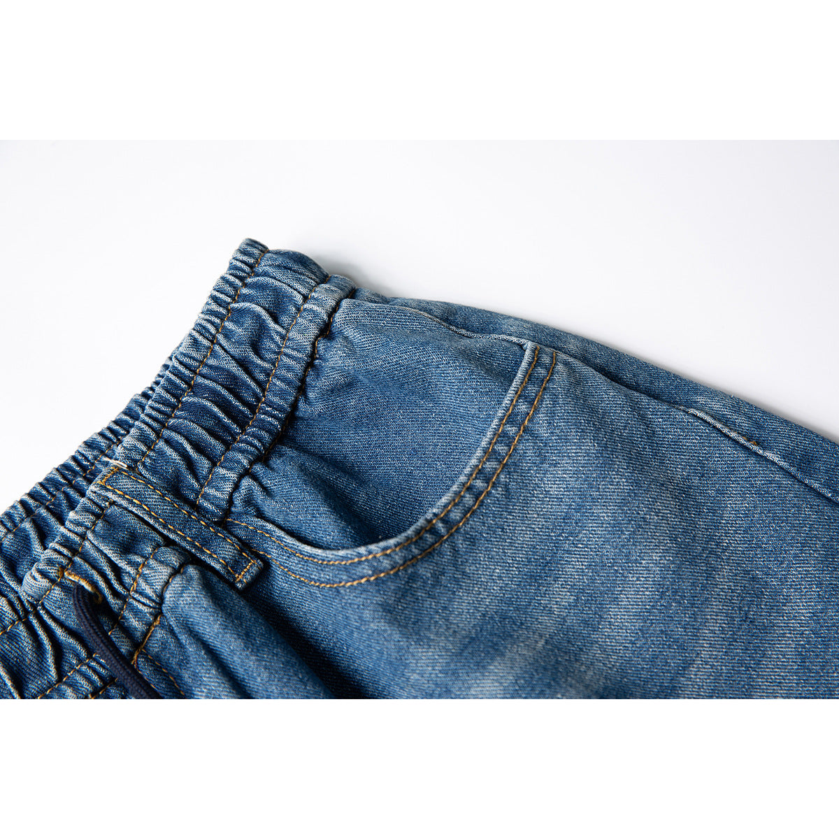 Close-up of blue denim pants showing the elastic waistband and curved front pocket with contrast stitching.