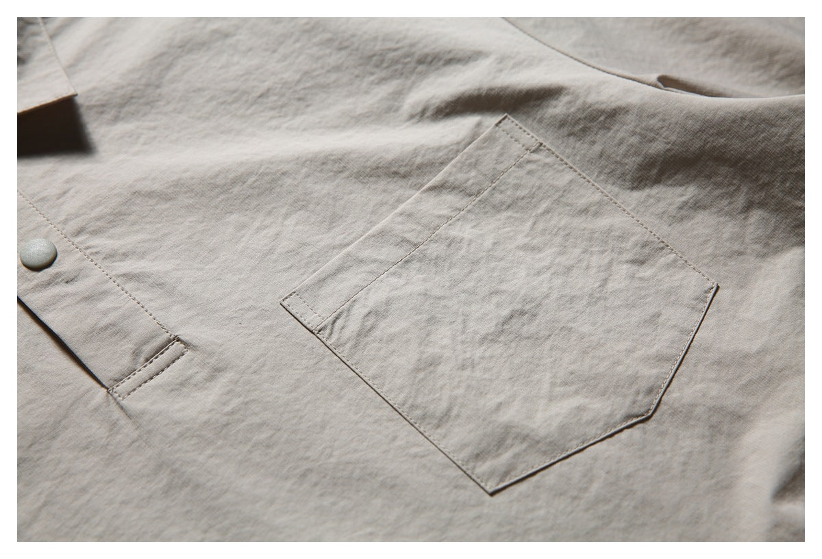 Close-up of a light taupe shirt showing a large patch pocket, a button, and stitched placket.