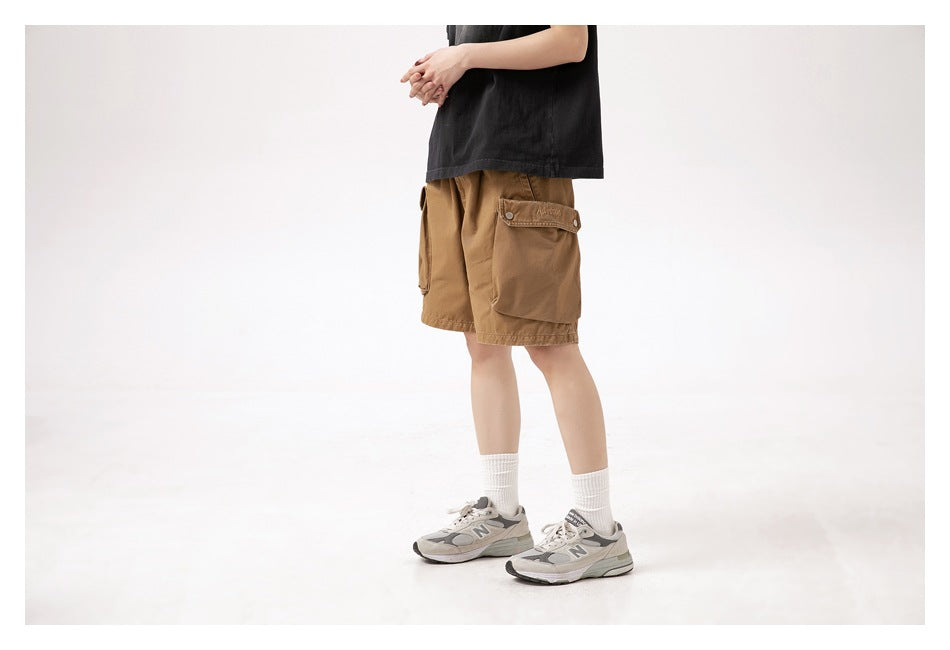 Model in brown cargo shorts, shown from the side with flap pockets, a black T-shirt, white socks and sneakers.