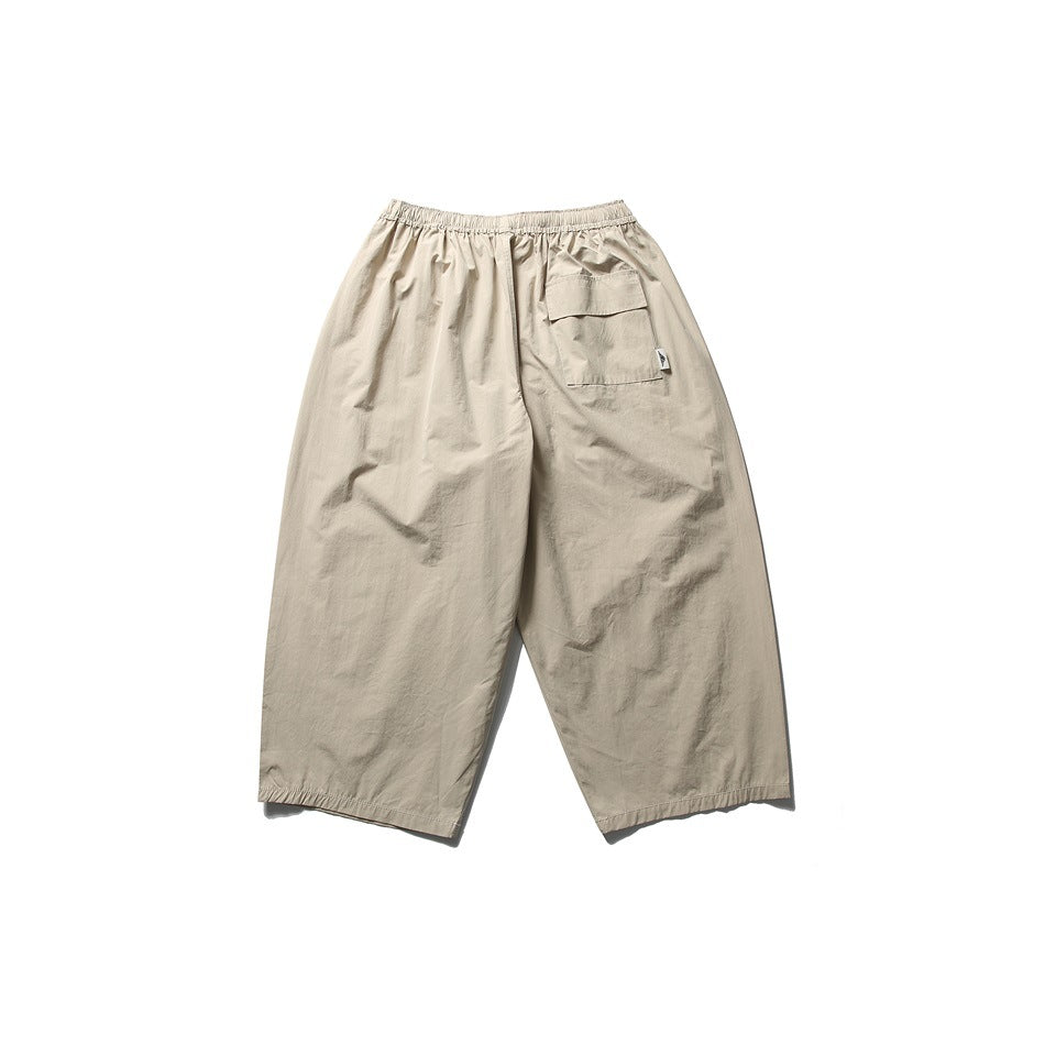 Rear view of loose light beige pants with an elastic waistband and a flap cargo pocket.