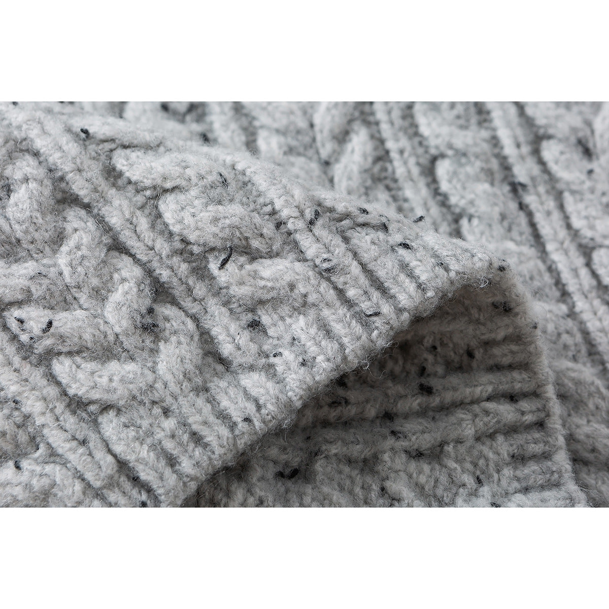 Close-up of folded light gray flecked cable-knit fabric, showing its raised stitches.