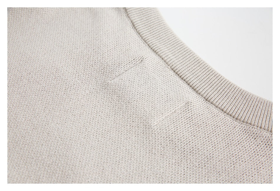 Close-up of a light beige knit garment with a ribbed neckline and visible shoulder seam.