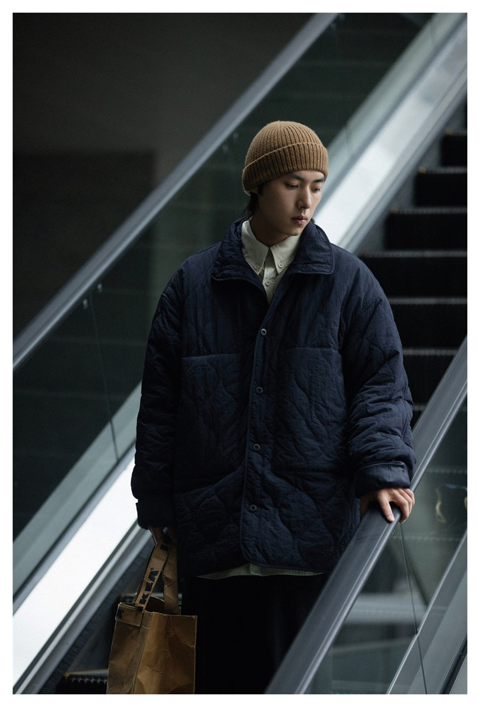 Model wearing a dark navy quilted button-front jacket over a pale shirt, with a brown ribbed beanie.