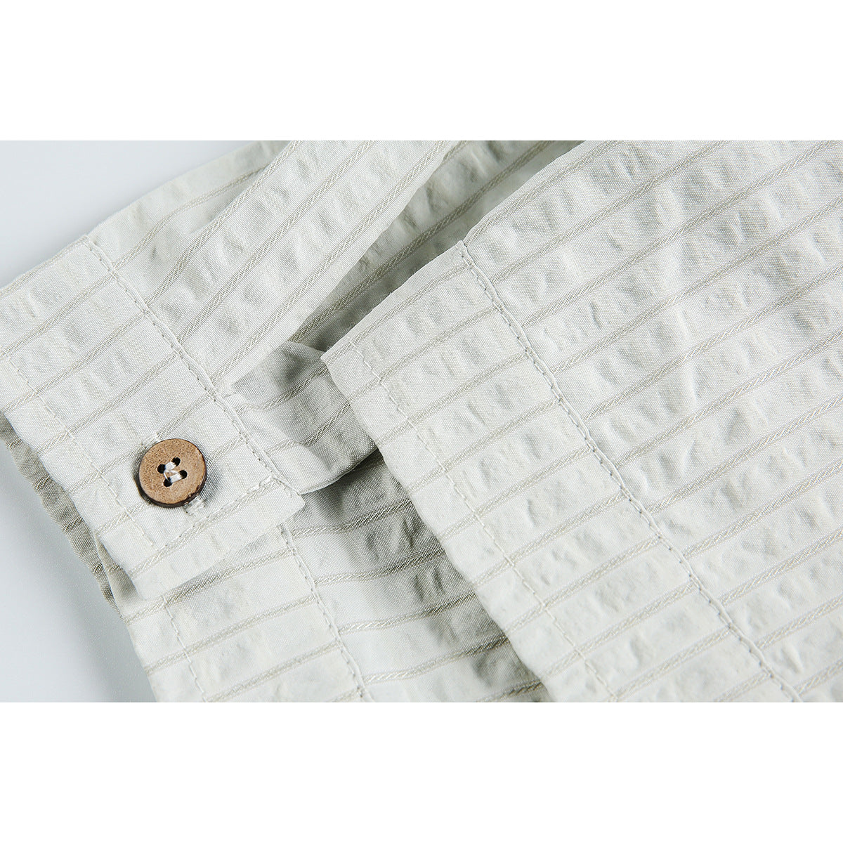 Close-up of a white shirt cuff with a brown button and textured striped fabric.