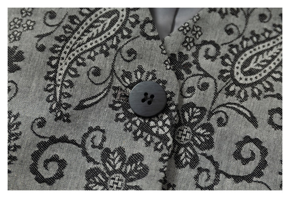 Close-up of a dark four-hole button against the jacket's gray and black paisley fabric.
