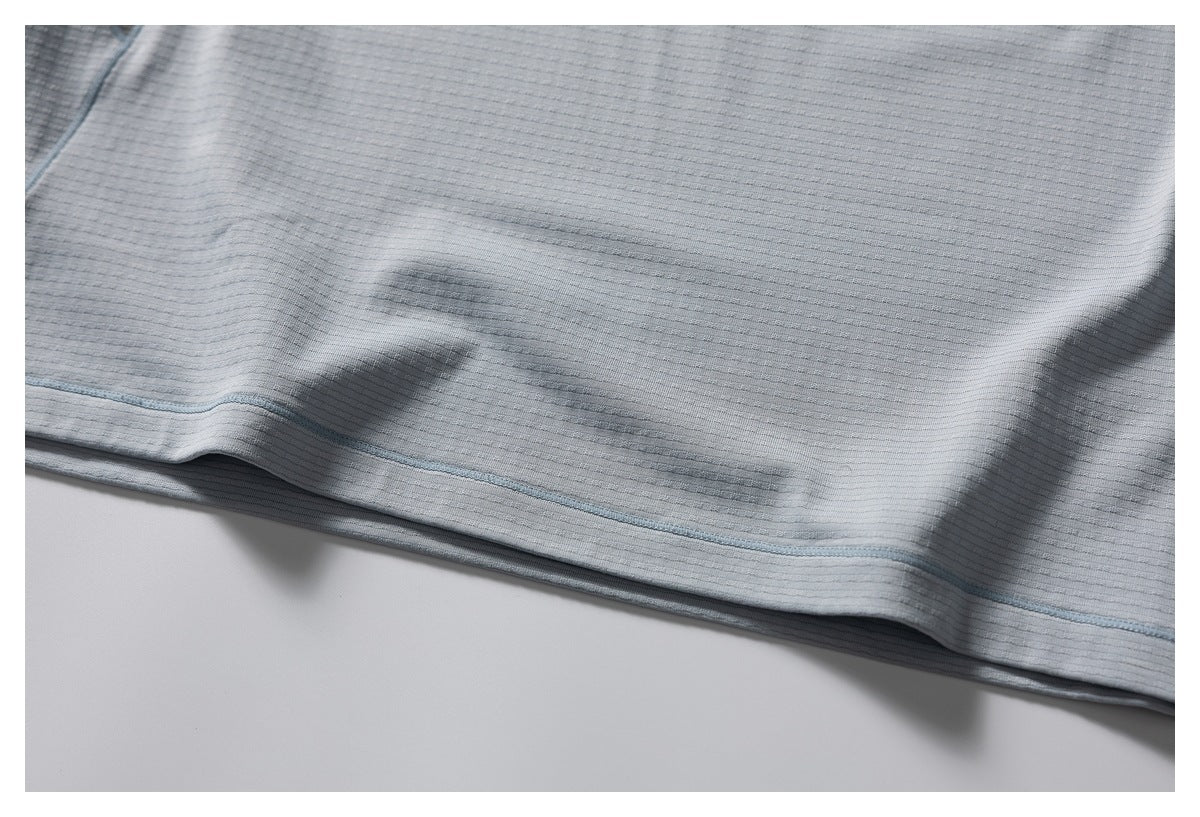 Close-up of the light gray-blue shirt’s textured fabric and stitched lower hem.