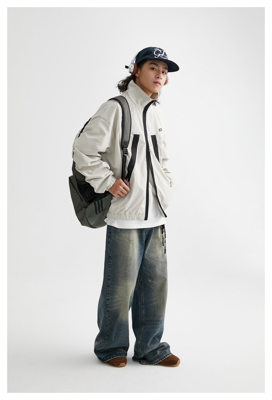 Full-length model wearing the light gray and black jacket with loose jeans and carrying a dark shoulder bag.