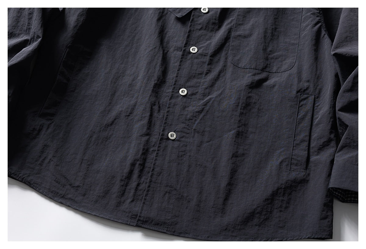 Cropped front of a dark charcoal button-up shirt with a chest pocket, side pockets, and curved hem.