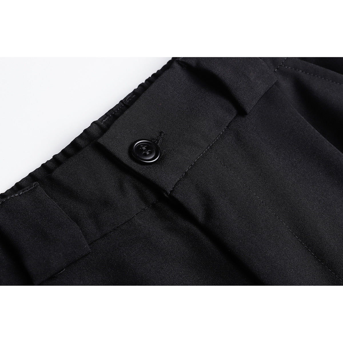 Close-up of black trousers showing the waistband, belt loop, button, and stitching.