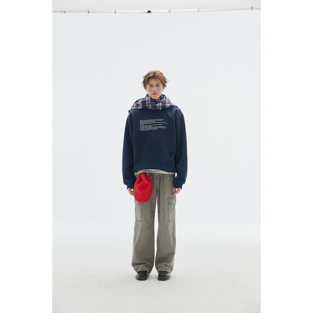 Model wearing a navy graphic sweatshirt, gray cargo pants, and a plaid scarf.