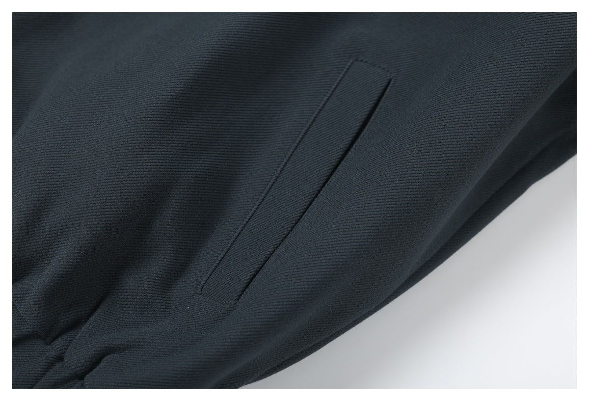 Close-up of a narrow vertical welt pocket on dark charcoal fabric.