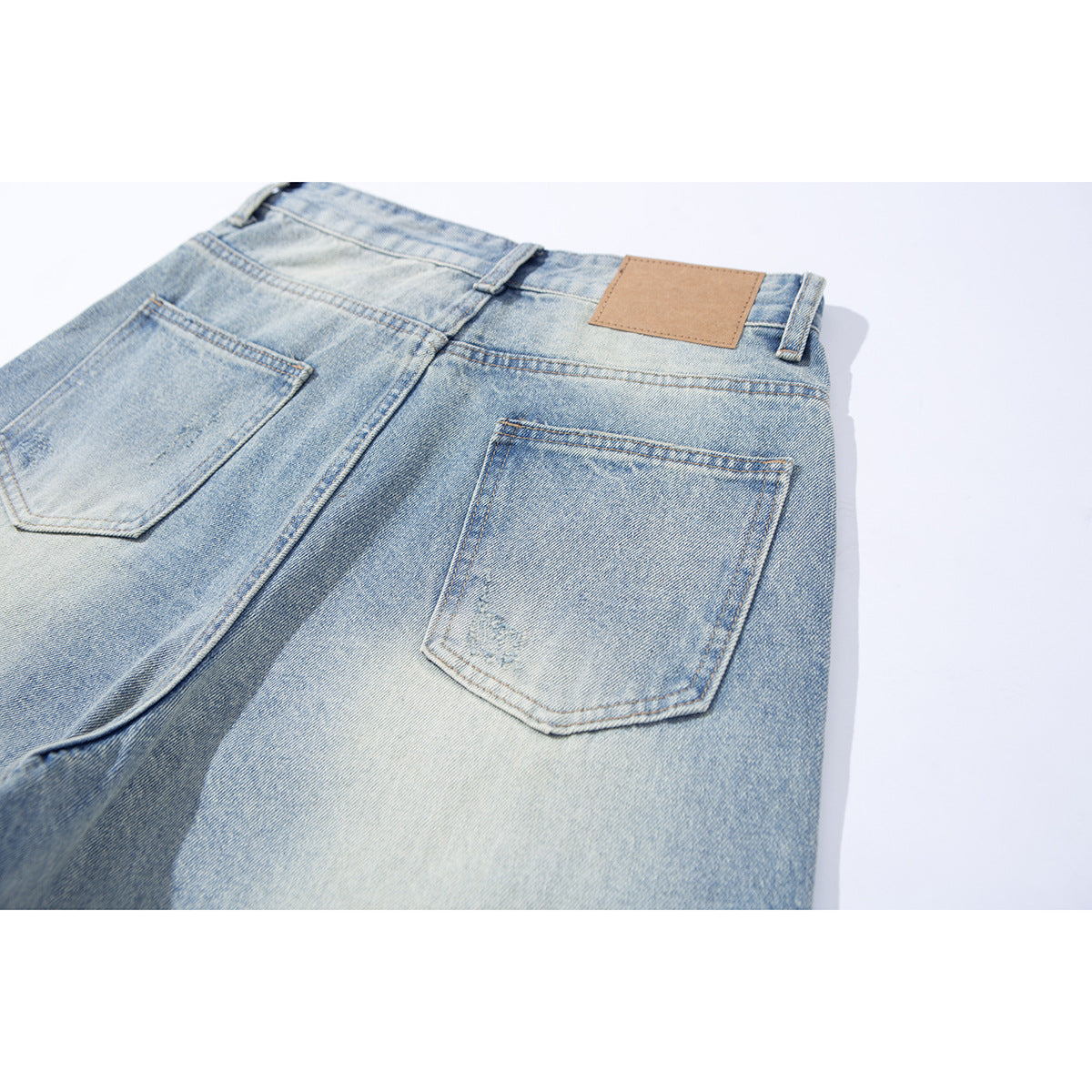 Close-up of the back of light-wash jeans with two pockets and a blank tan waistband patch.