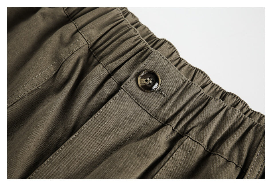 Close-up of an olive trouser waistband with elastic gathers, stitching and a dark button closure.