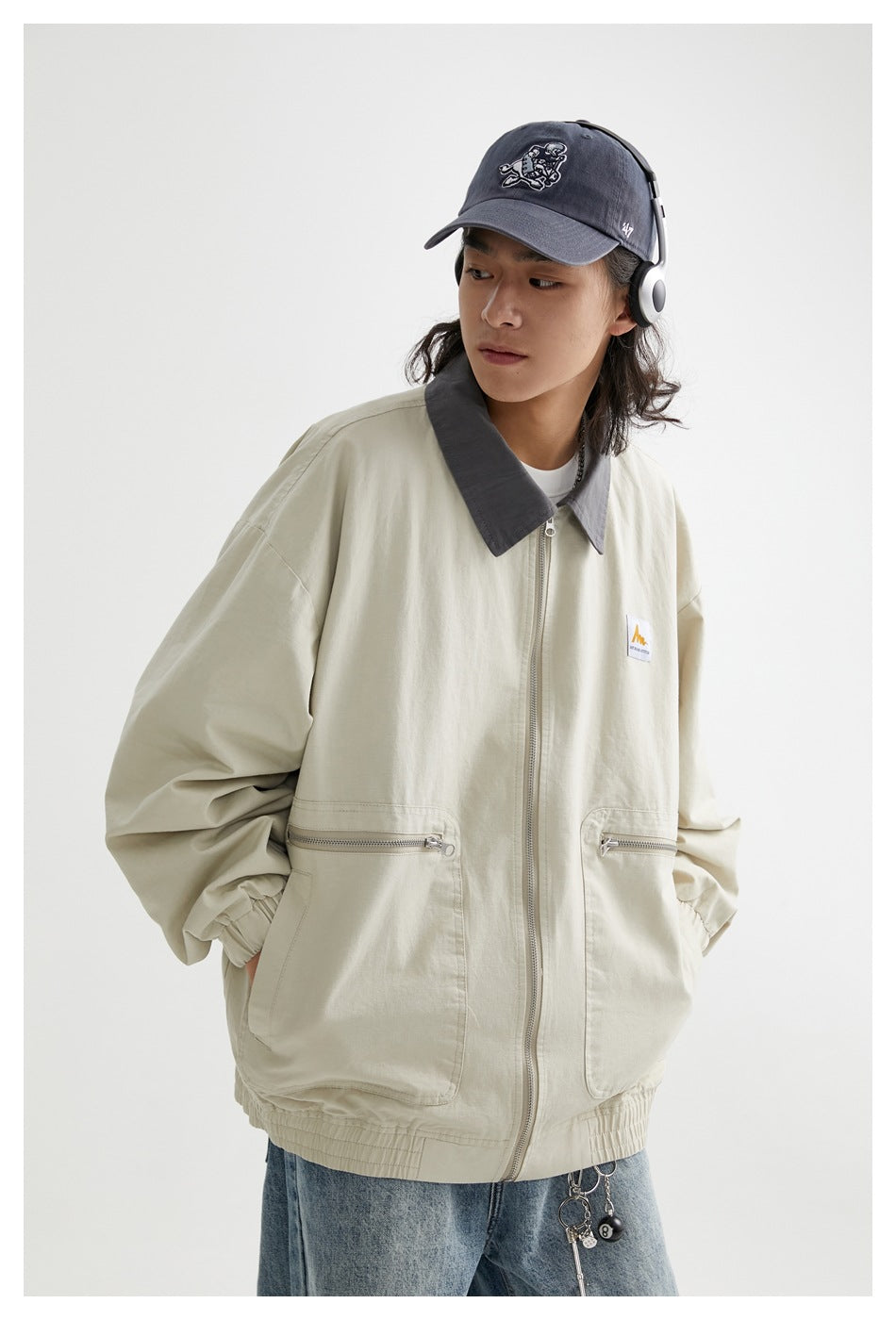 Three-quarter view of a model wearing a light khaki jacket with a gray collar and zippered front pockets.