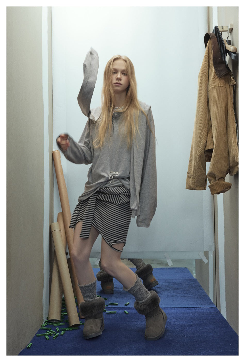 Model wearing a loose gray top and black-and-gray striped skirt, with a gray sleeve raised as she poses.