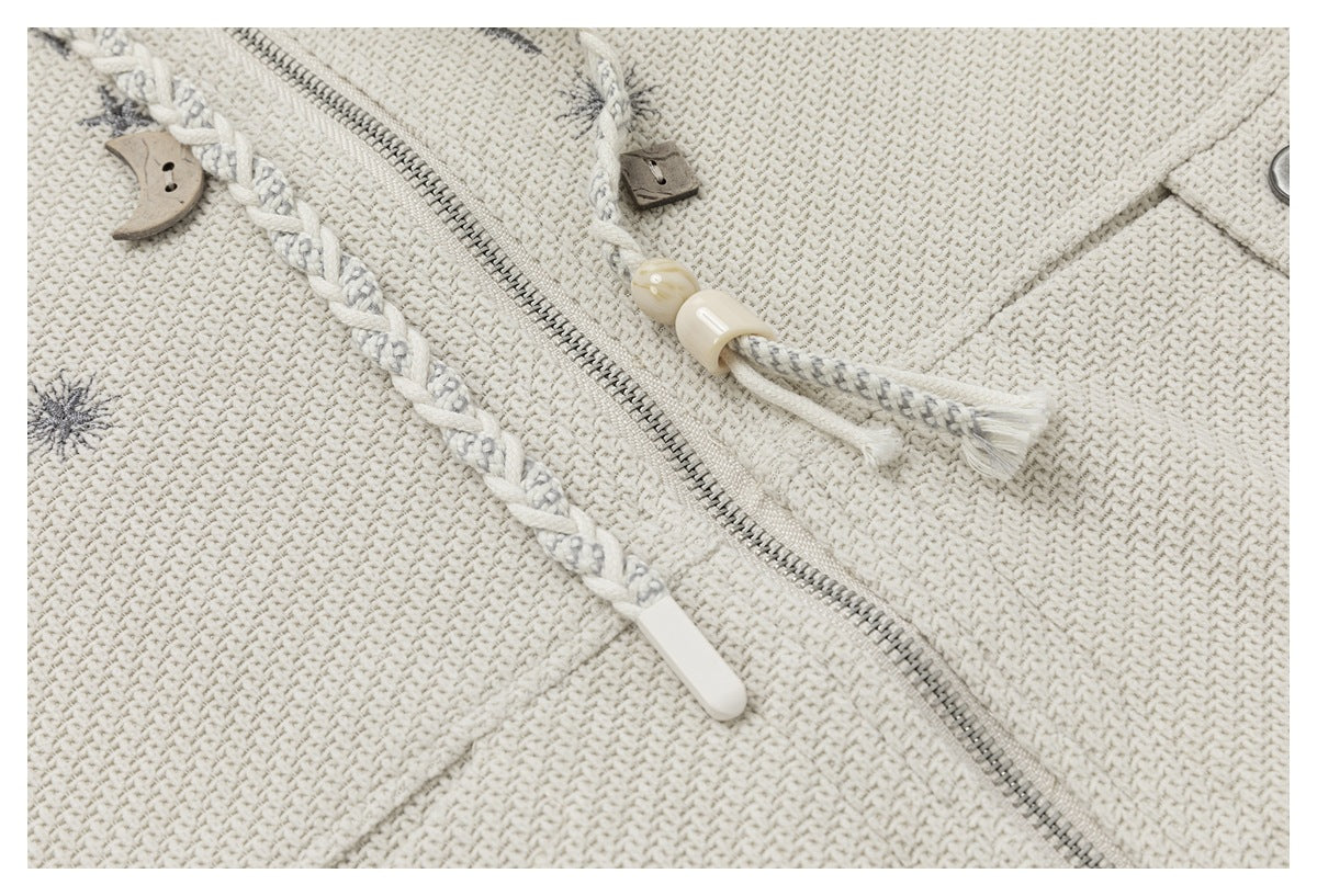 Close-up of an ivory jacket showing a metal zipper, braided drawcords, and decorative toggles.