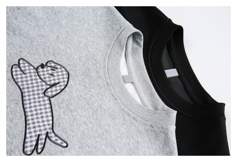 Close-up of gray and black crewneck tees, showing a gingham dog appliqué and the neckline details.