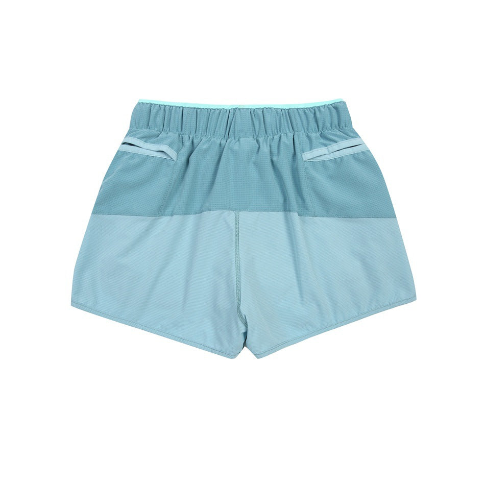Back view of color-block athletic shorts in teal and pale aqua with an elastic waistband and angled pocket openings.