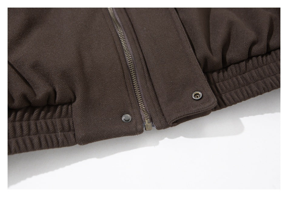 Close-up of a dark brown garment with a front zipper, snap fasteners, and gathered elastic hem.