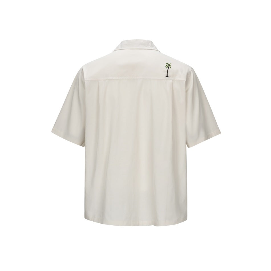 Back view of beige short-sleeve shirt with a small embroidered palm tree on the upper back yoke