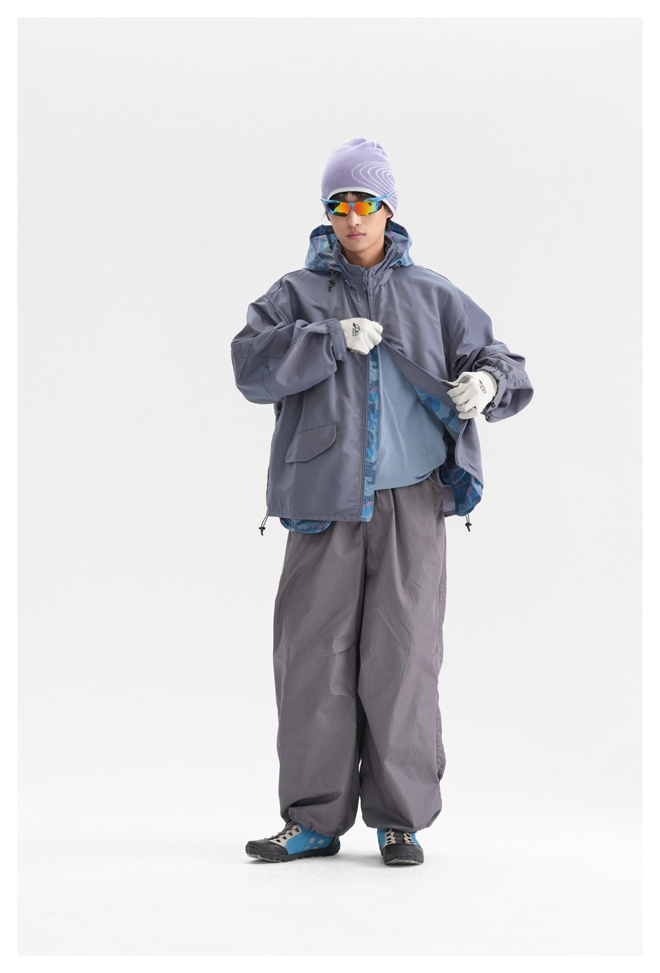 Full-length model wearing a slate gray hooded jacket with blue patterned lining, loose gray pants and a lavender beanie.
