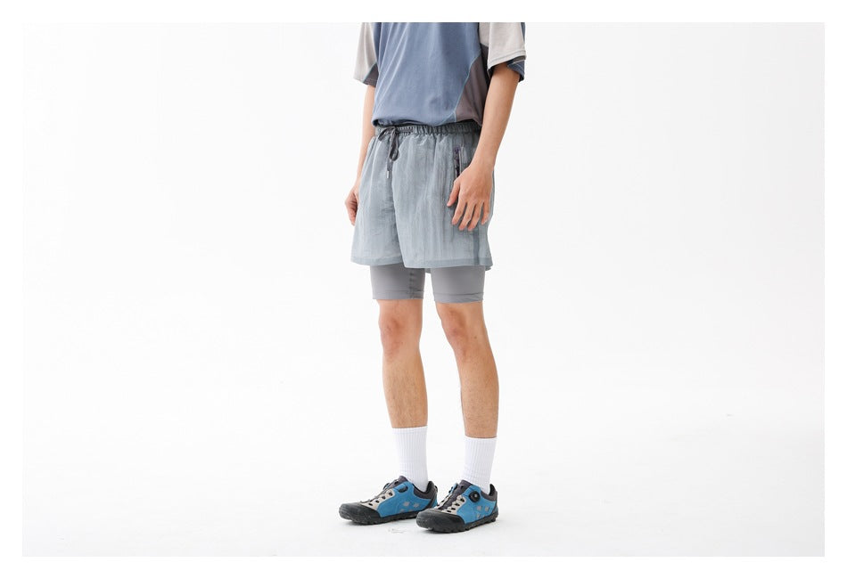 Three-quarter view of a person wearing light gray-blue running shorts over gray compression shorts.