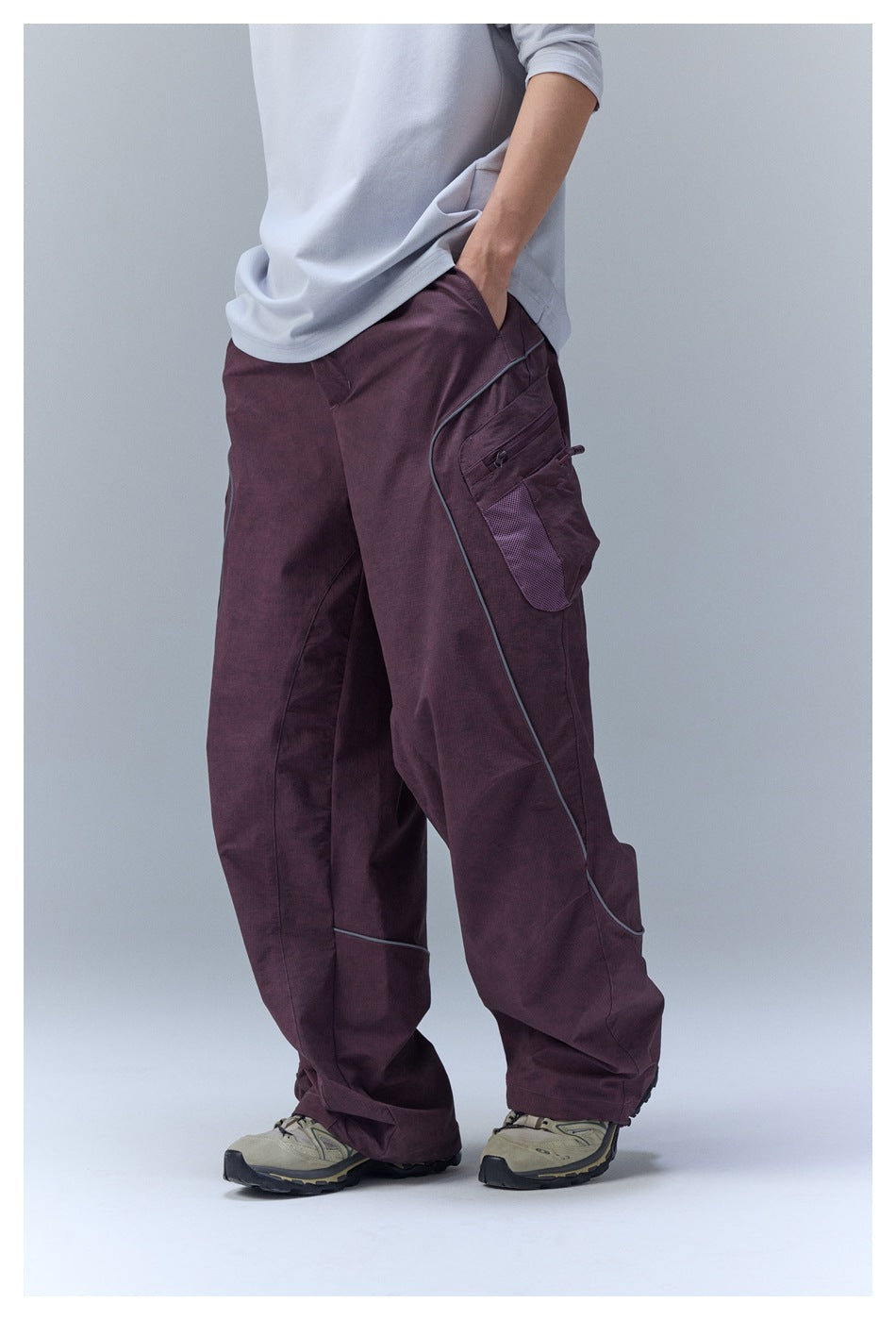 Side view of person in purple wide-leg cargo pants showing zippered mesh side pocket and curved piping