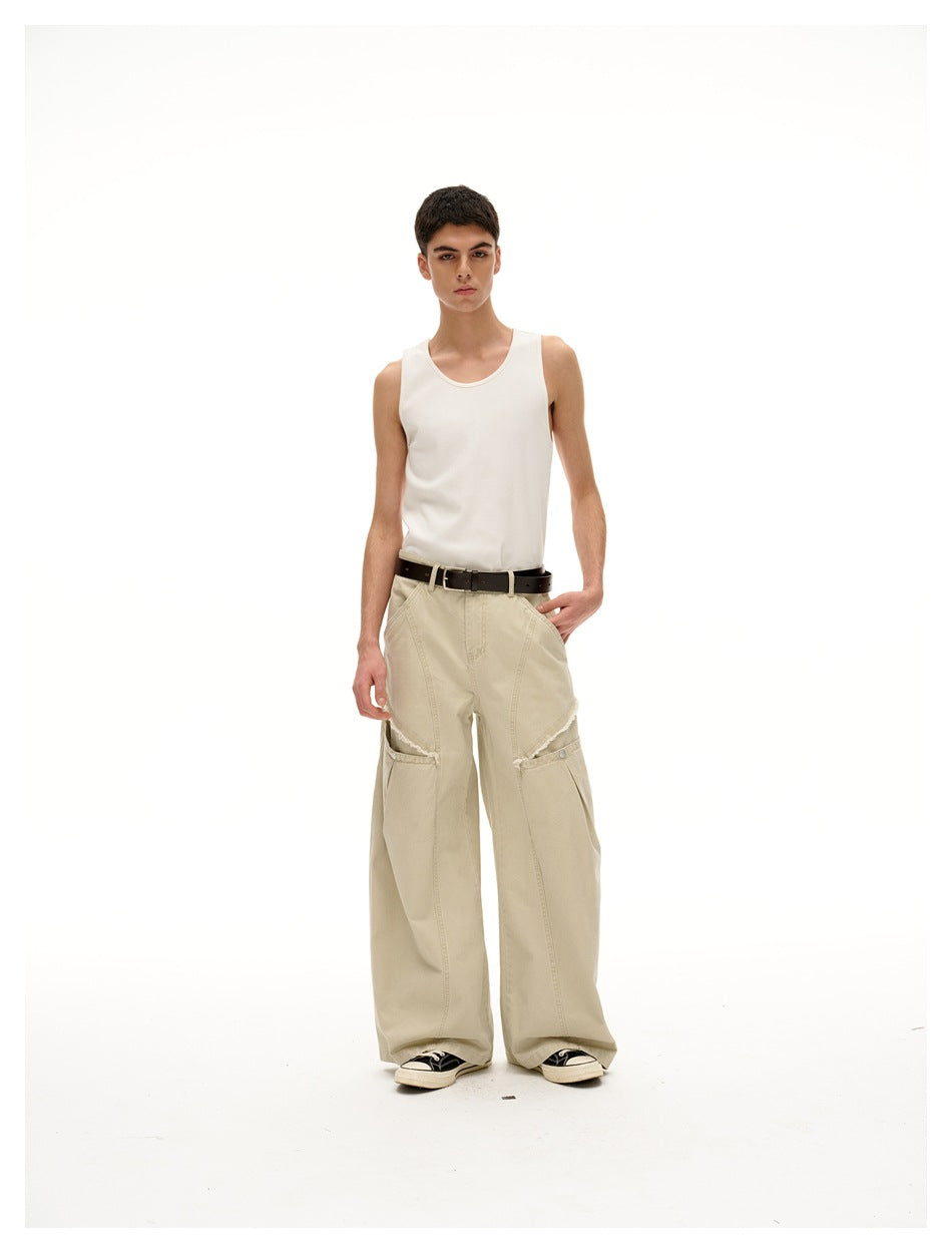 Model wearing light khaki wide-leg pants with frayed thigh slits, a white tank top, brown belt and sneakers, front view