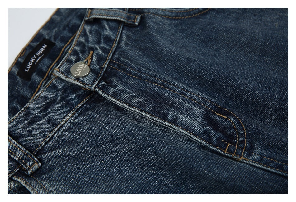 Close-up of dark blue jeans with a front pocket, belt loop, metal button and sewn black label.