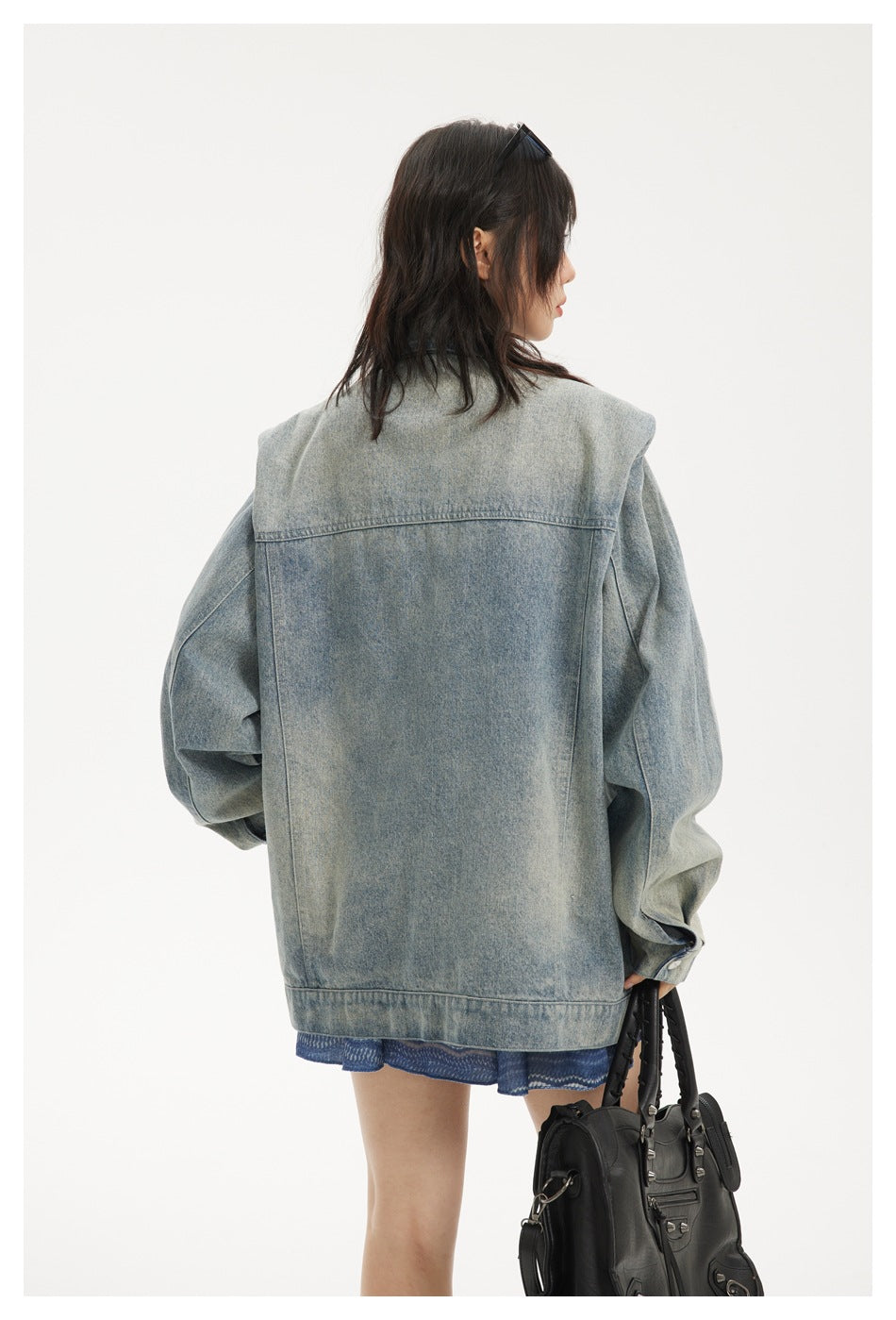 Close rear view of the oversized faded blue denim jacket, showing its back yoke, seams, and wide hem.