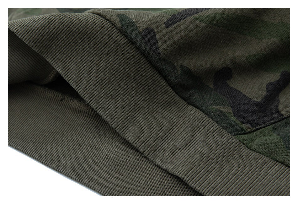 Close-up of a dark olive ribbed sweatshirt hem beside green camouflage fabric.