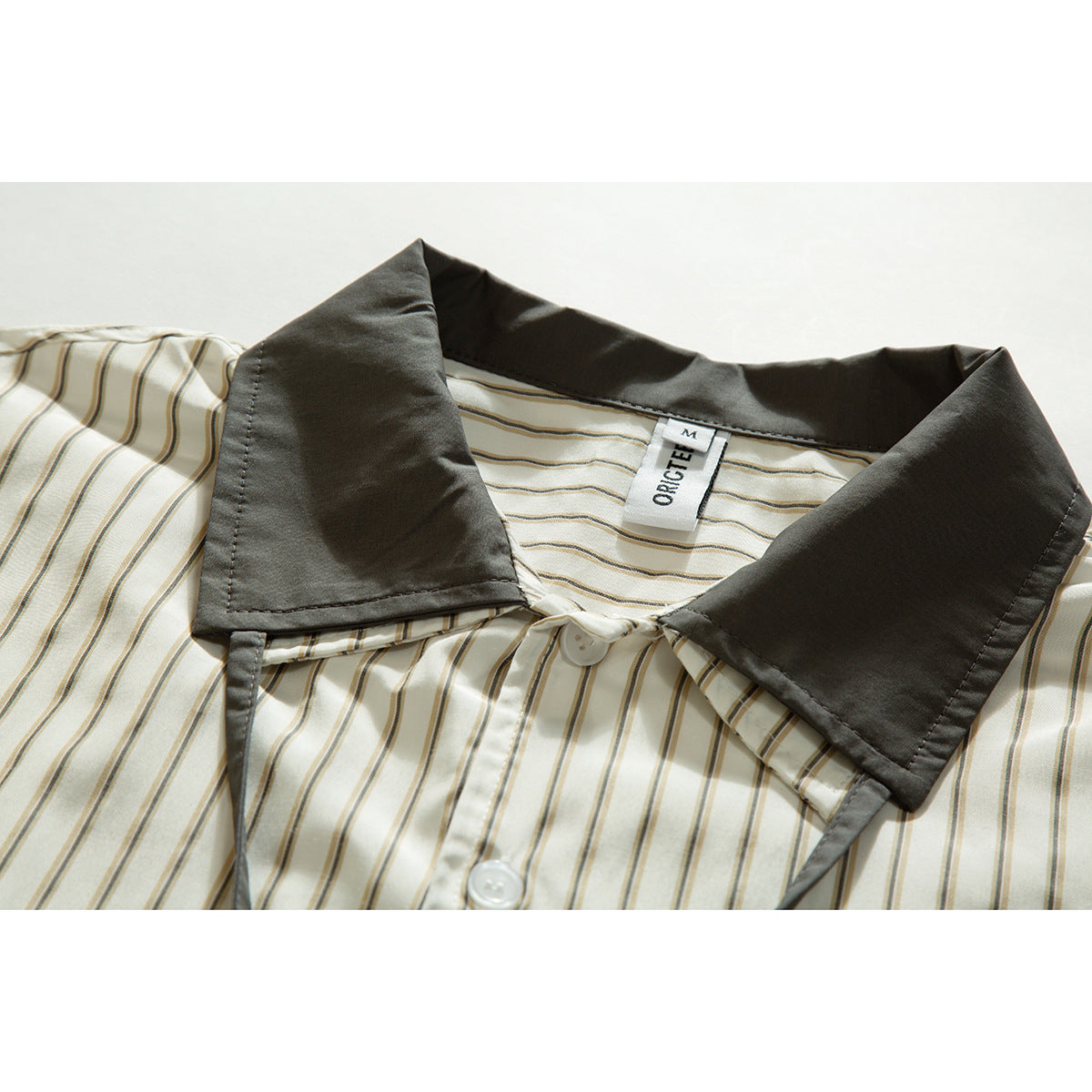 Close-up of a cream striped shirt collar with dark charcoal-gray collar panels and a visible neck label.