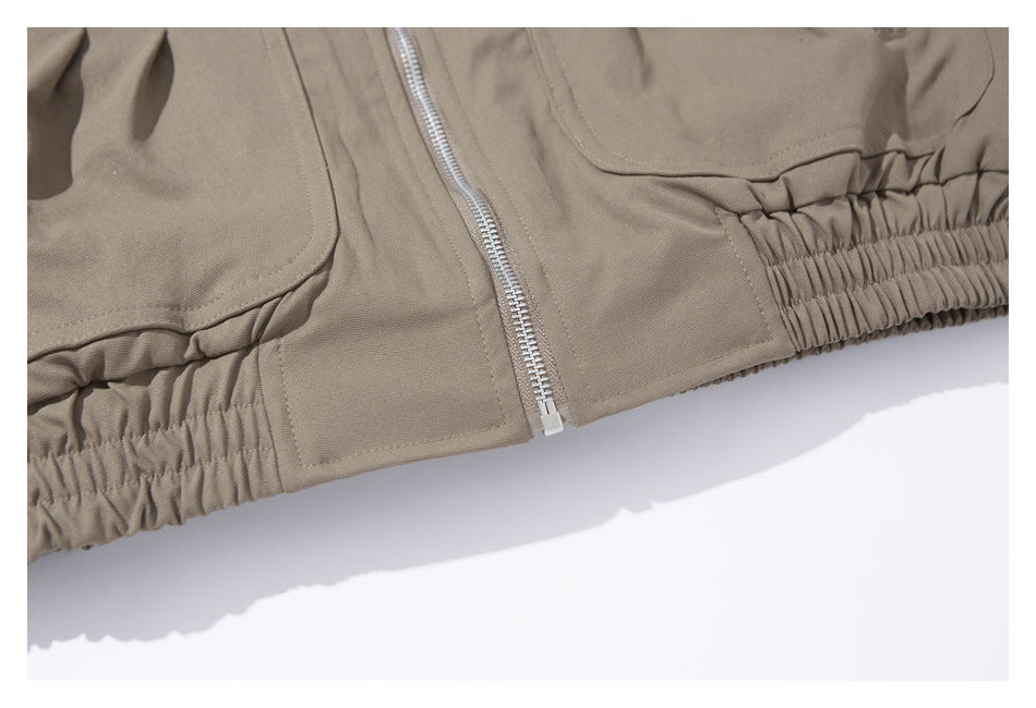 Close-up of the taupe jacket's silver front zipper and gathered elastic hem.