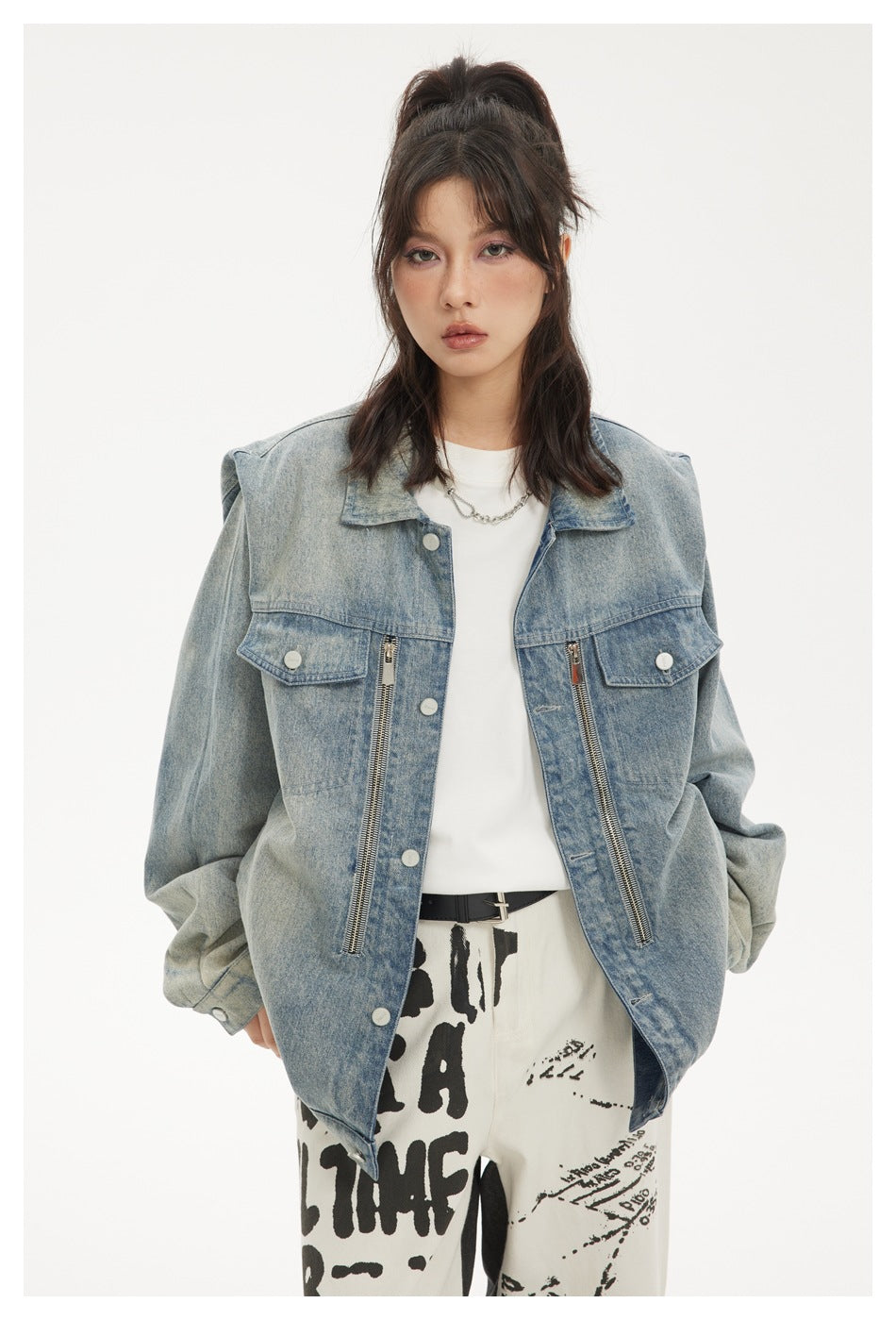 Model wearing an open, oversized light-wash denim jacket with snap buttons, flap pockets and long front zippers.