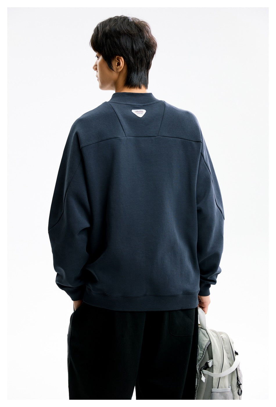 Back view of a model in a navy sweatshirt with ribbed collar, back yoke seams and a small triangular label