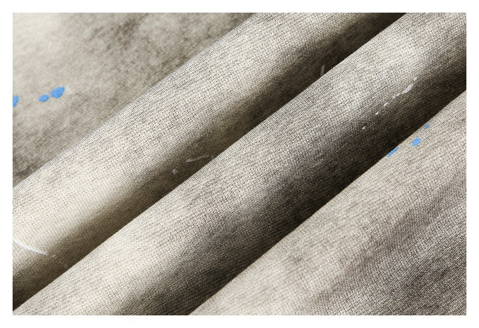Close-up of folded gray-beige fabric showing its mottled surface and scattered white and blue marks.