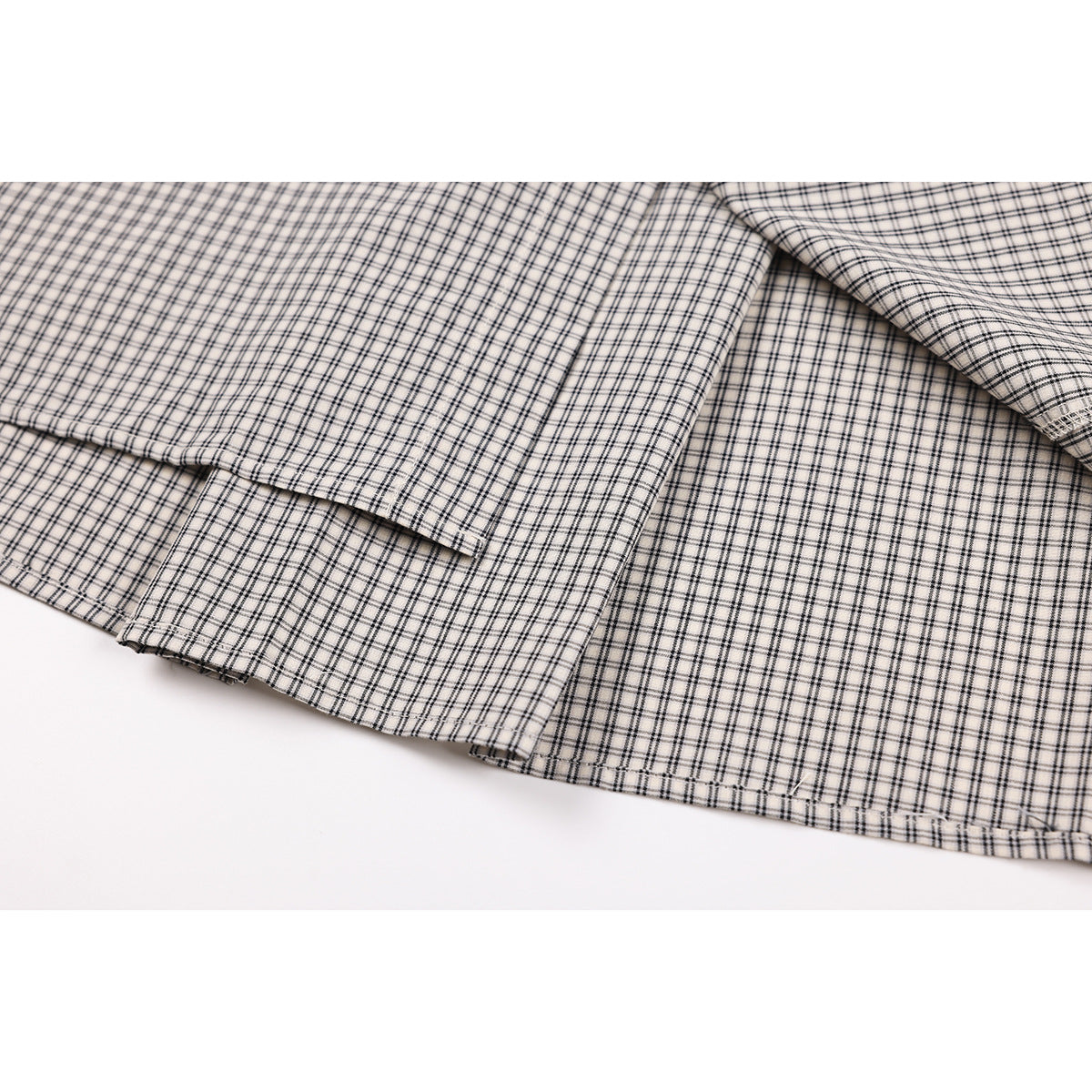 Close-up of the checked shirt's stitched hem and overlapping fabric panels.