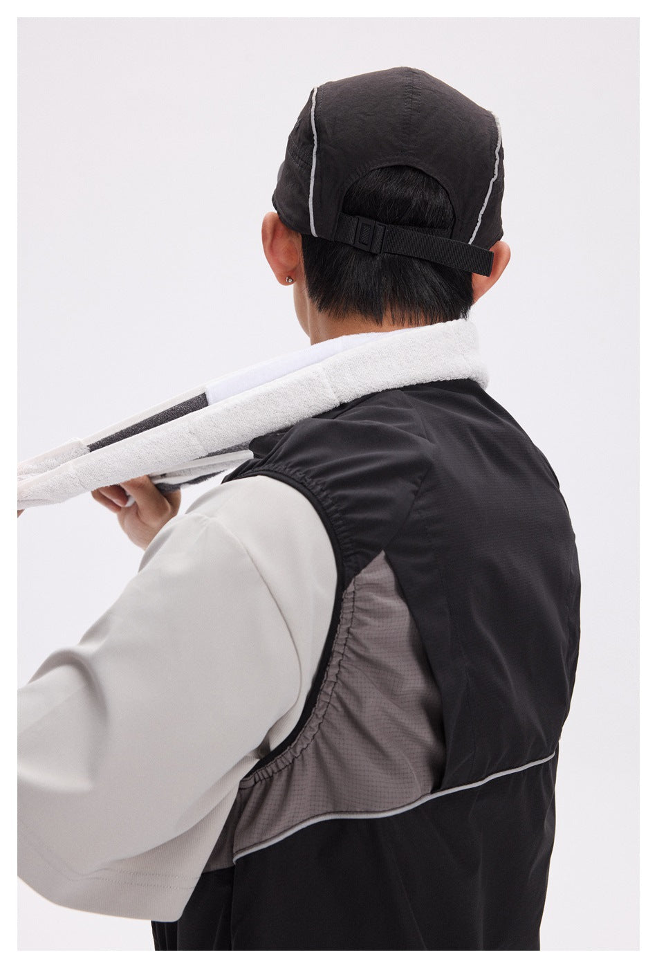 Close rear-side view of a black vest, showing gray mesh side panels and thin white piping.