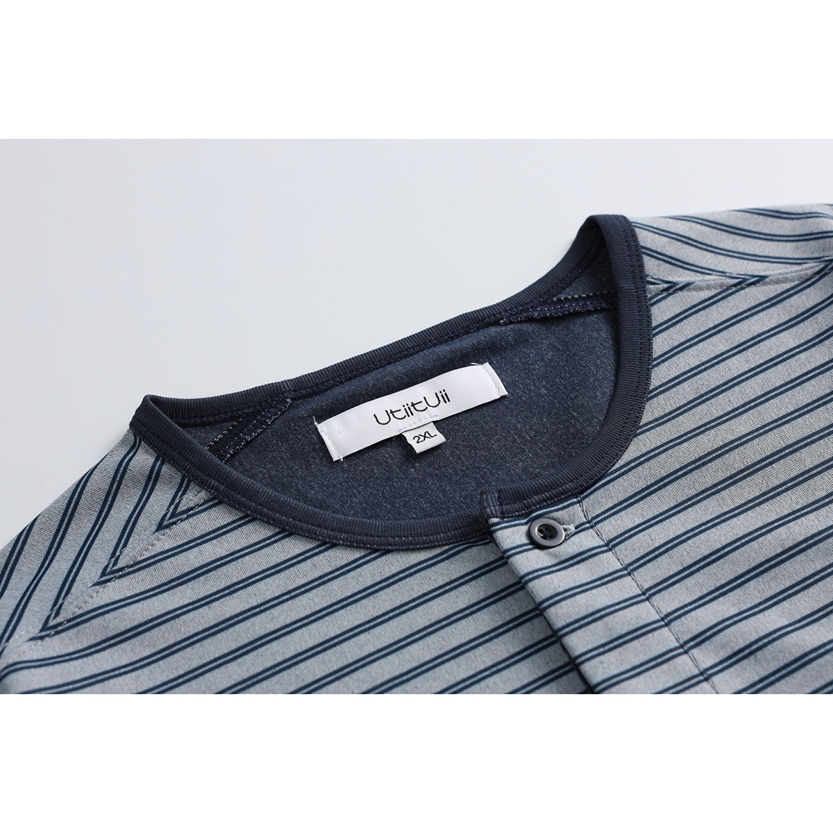 Close-up of a blue-gray striped shirt neckline, dark trim, button placket, and sewn-in label.