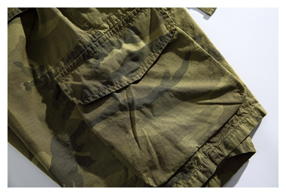 Close-up of a flap cargo pocket and leg hem on olive camouflage shorts.