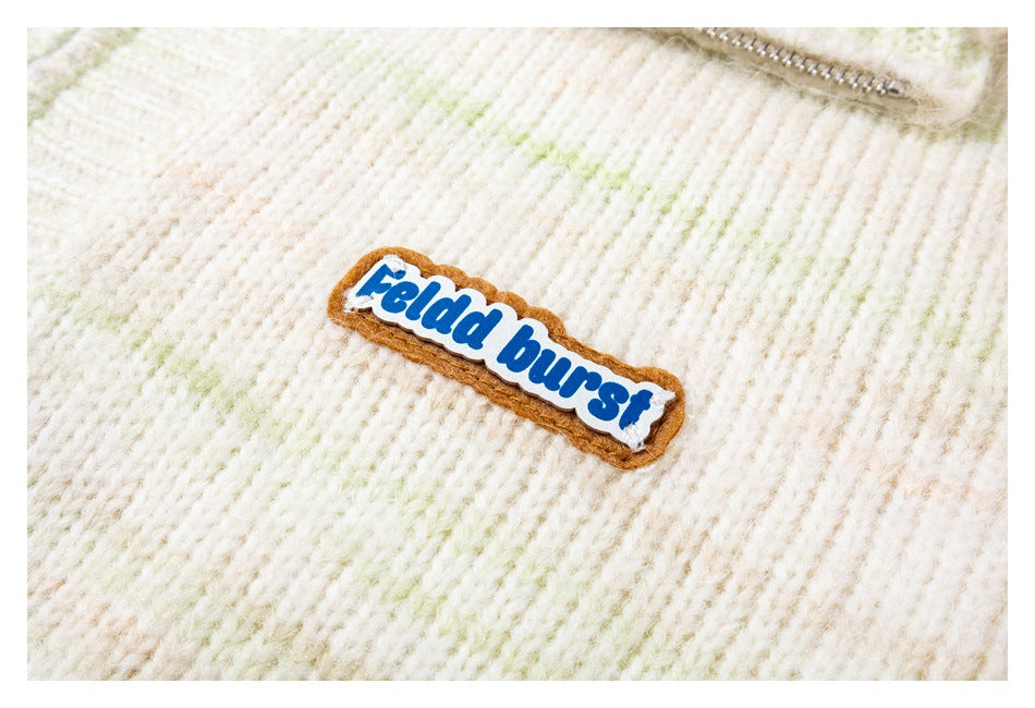 Close-up of a colorful sewn brand patch on the ivory sweater's lightly streaked knit fabric.