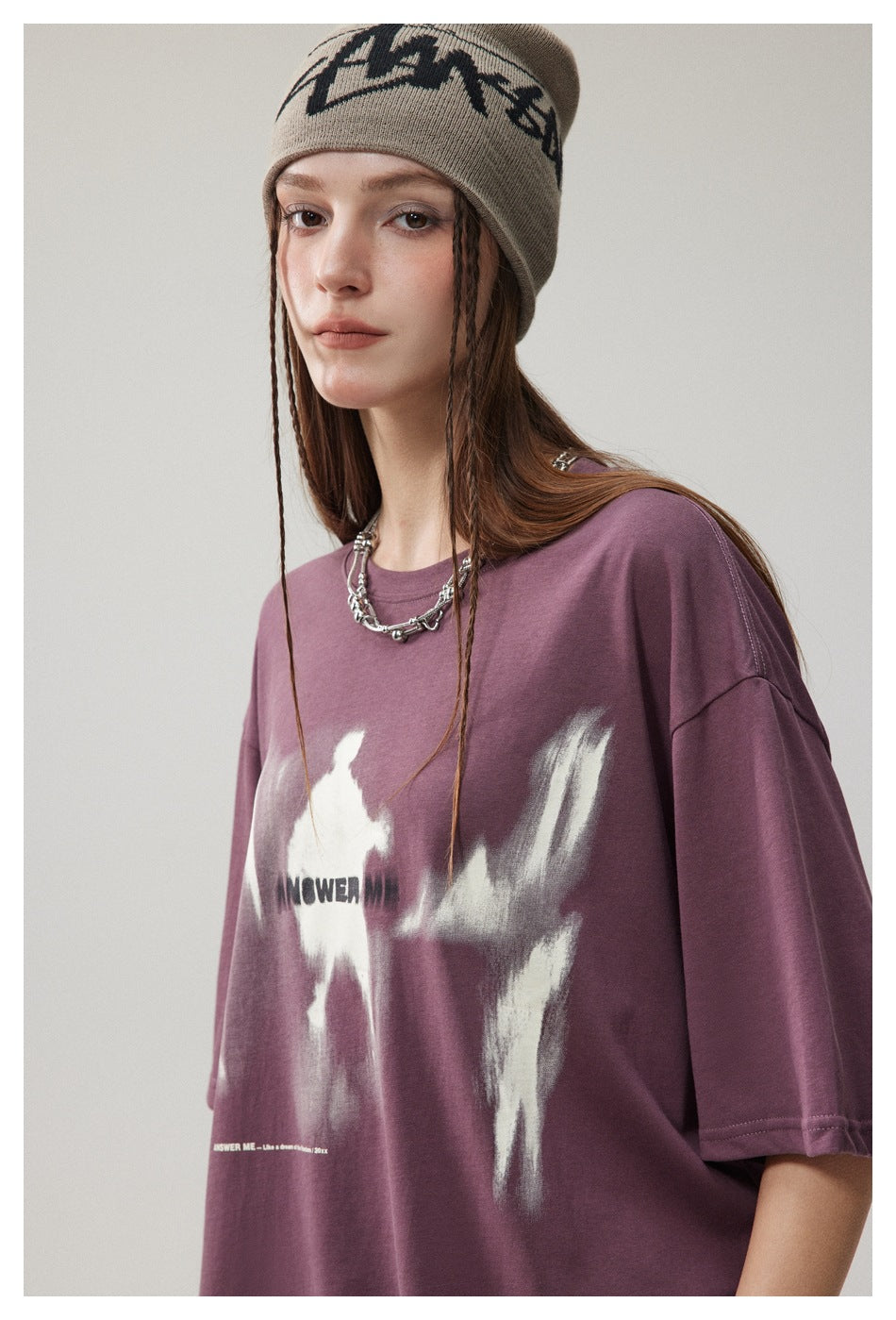 Model wearing a taupe graphic beanie and oversized plum T-shirt with a white abstract print.