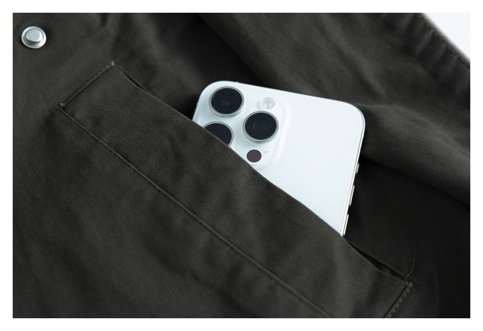 Close-up of a white phone tucked into a large pocket on a dark charcoal garment.