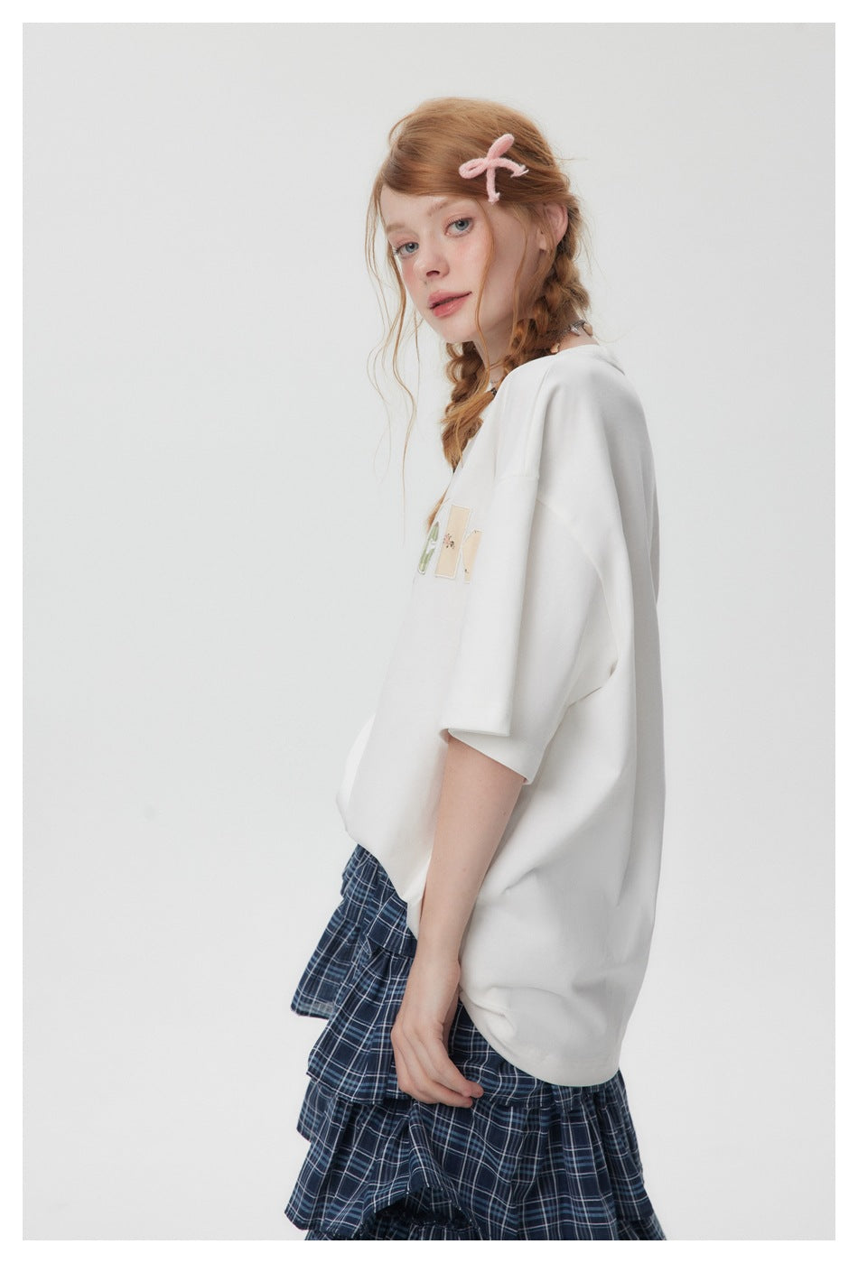 Side view of a model wearing an oversized white T-shirt with colorful chest lettering and a navy plaid tiered skirt.