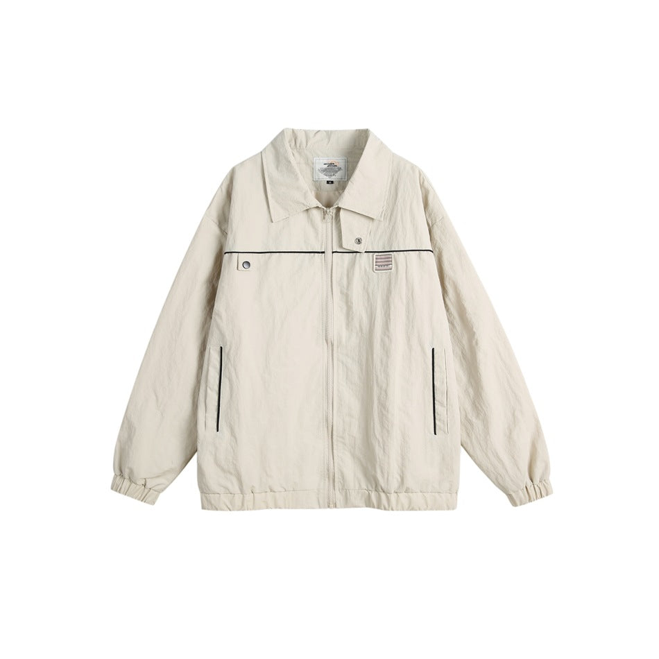 Beige zip-front jacket with turn-down collar, black piping, chest patch, side pockets and elastic cuffs, flat lay