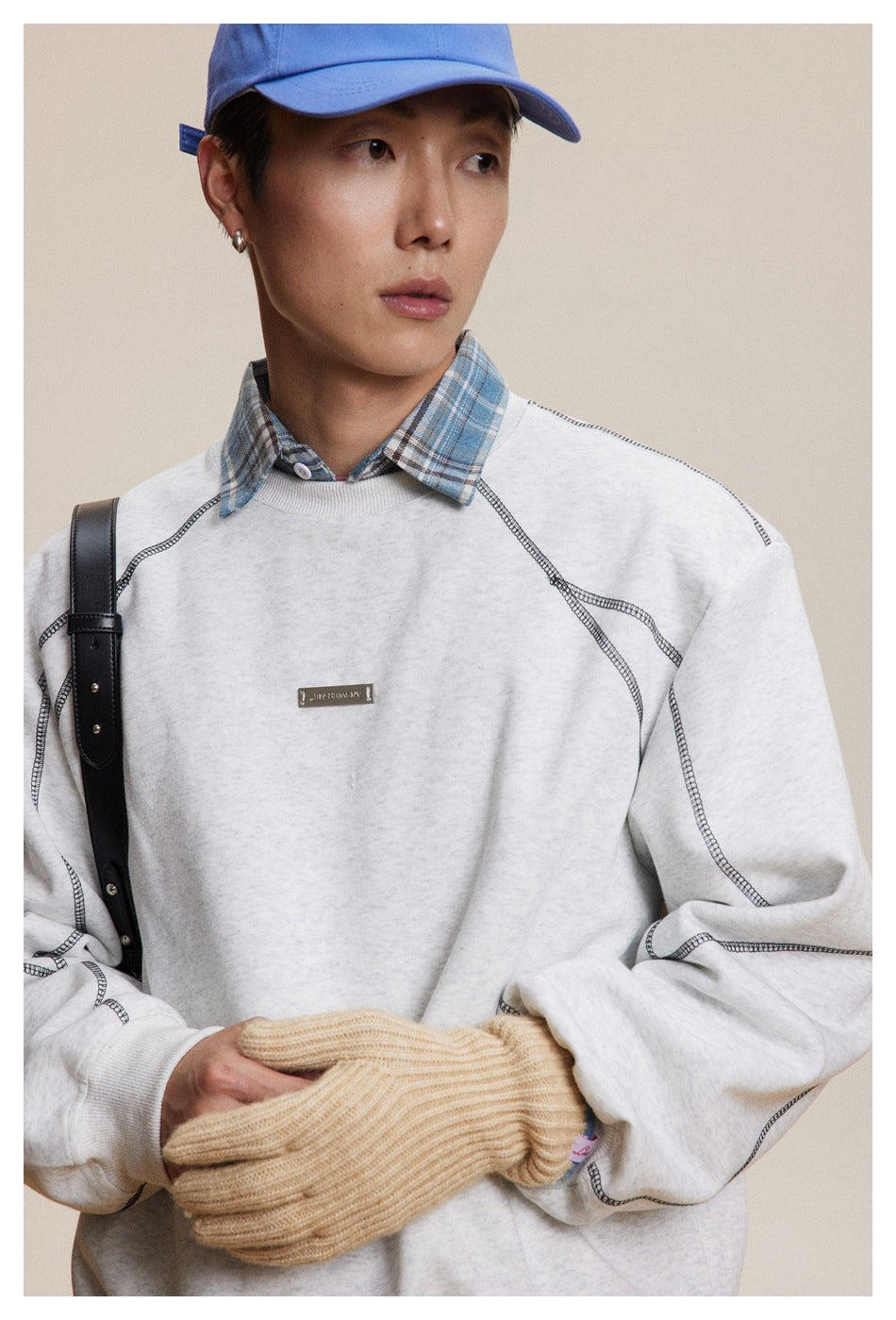 Close view of a model wearing a light gray sweatshirt with dark contrast seams and a blue plaid collar.