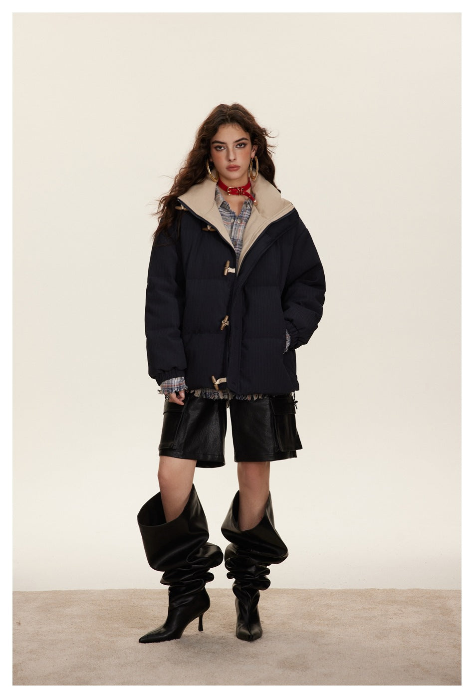 Model wearing a navy puffer jacket with toggle closures over a plaid shirt, leather shorts and tall black boots