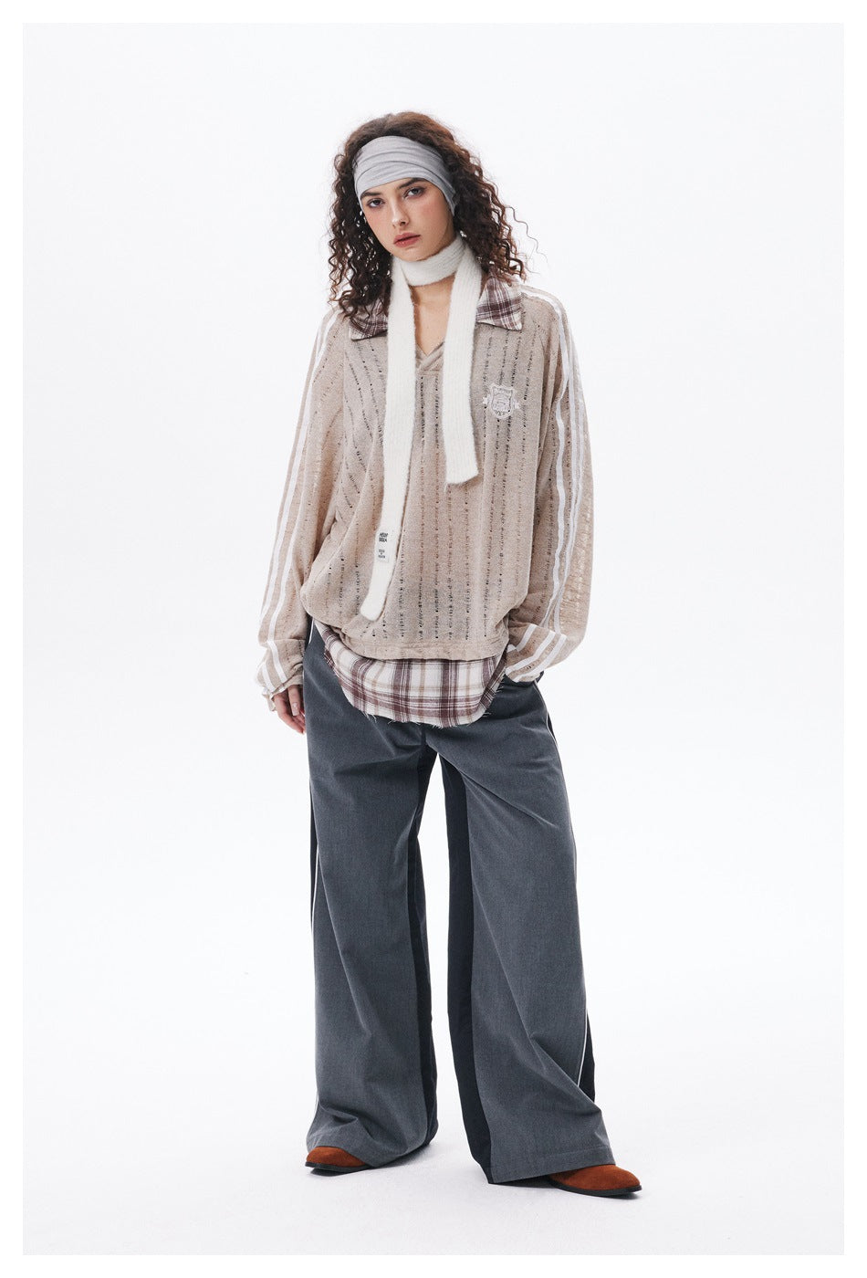 Full-length model in a beige striped open-knit pullover with plaid collar, white scarf, and dark wide-leg trousers.